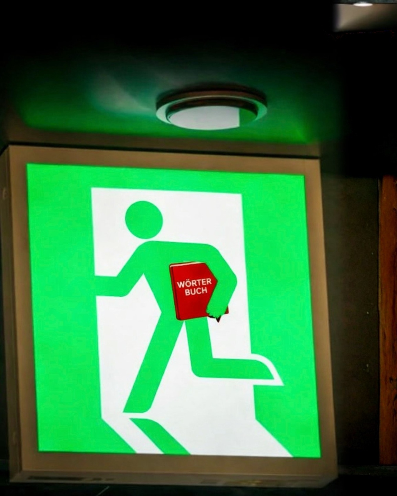 Grünes Notausgang-Männchen mit einem roten Wörterbuch unter dem Arm. KI-generiert.